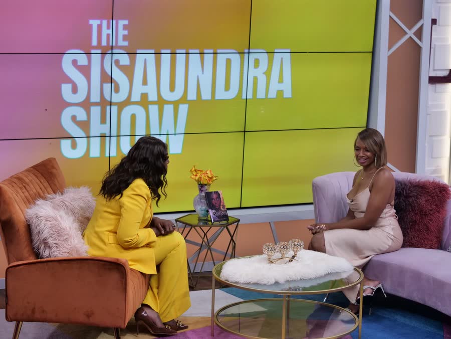 April on the Sisaundra Show set, BLAHOM staged in frame.